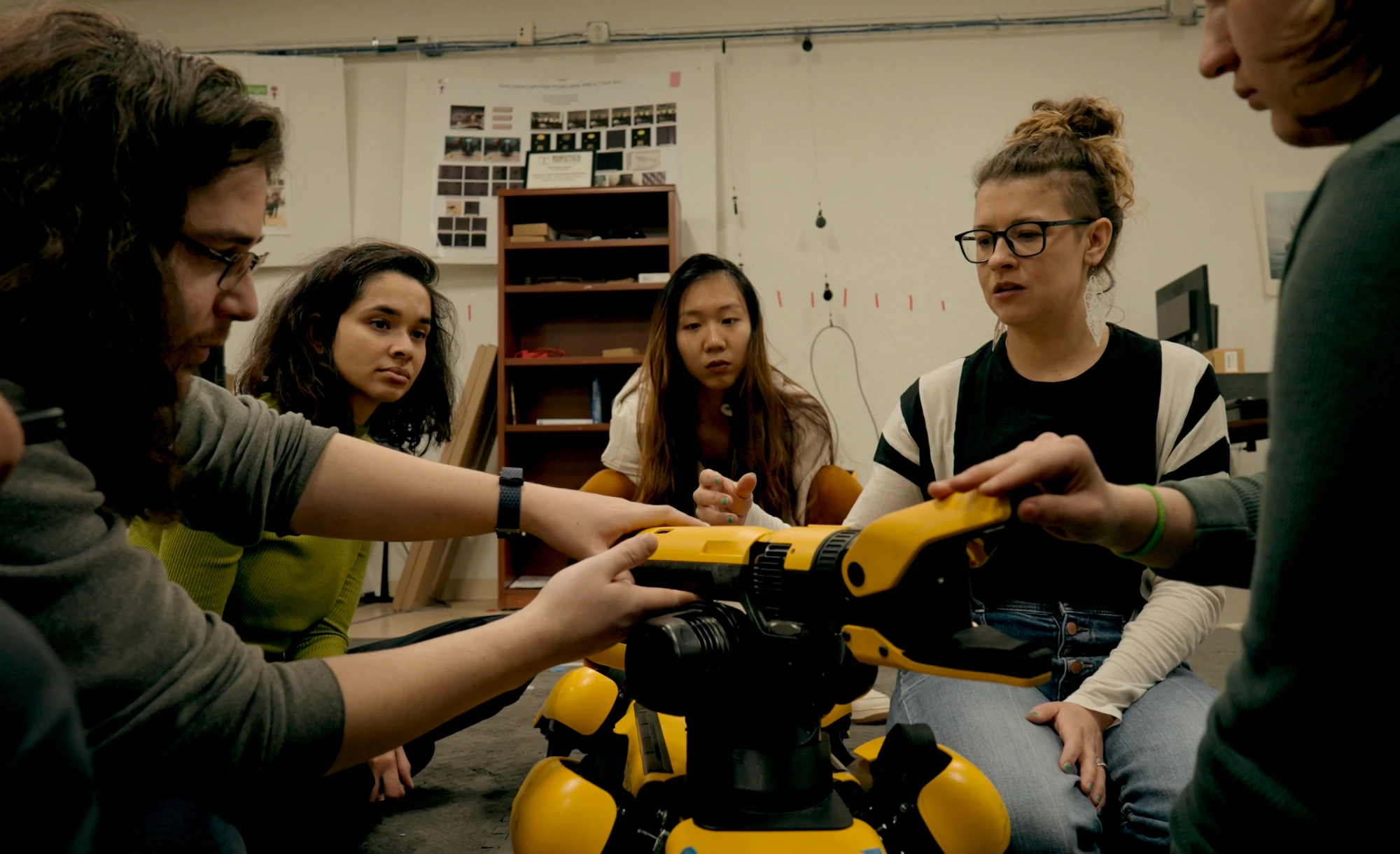 Five researchers seated on the floor around Spot, hands on the robot’s body and arm